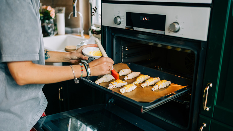 Person brushing croissants with egg wash as they go in an open oven