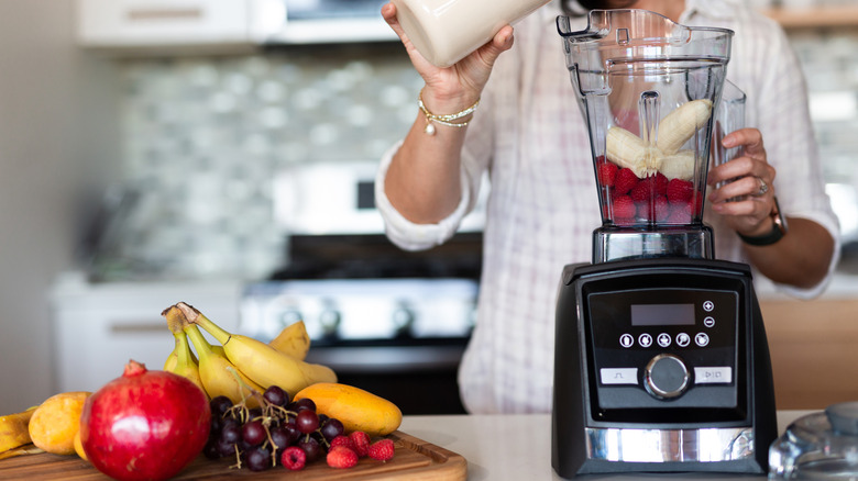 Someone making a fruit smoothie in a Vitamix with whole fruit placed alongside it
