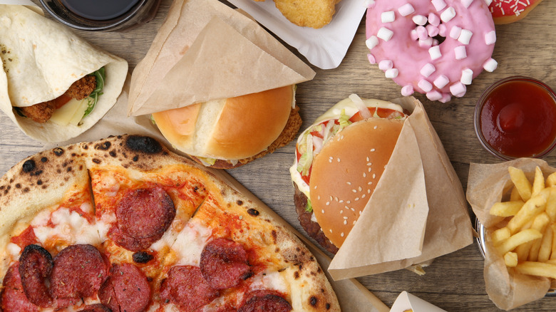 Pizza, burgers, tortilla wrap, fries, ketchup, and a pink donut displayed on a table