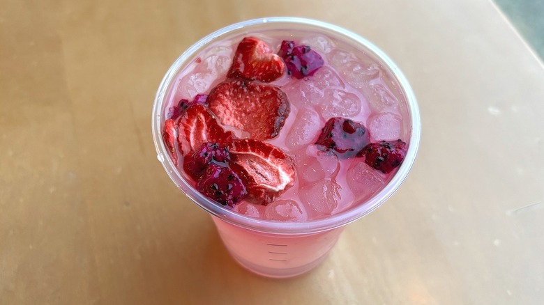 Top view of a light pink drink with floating strawberries and dragon fruit