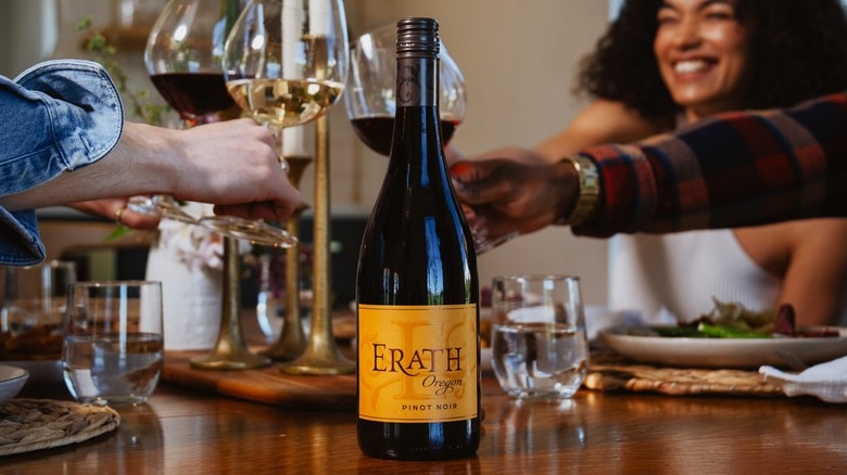 bottle of red wine with people clinking glasses