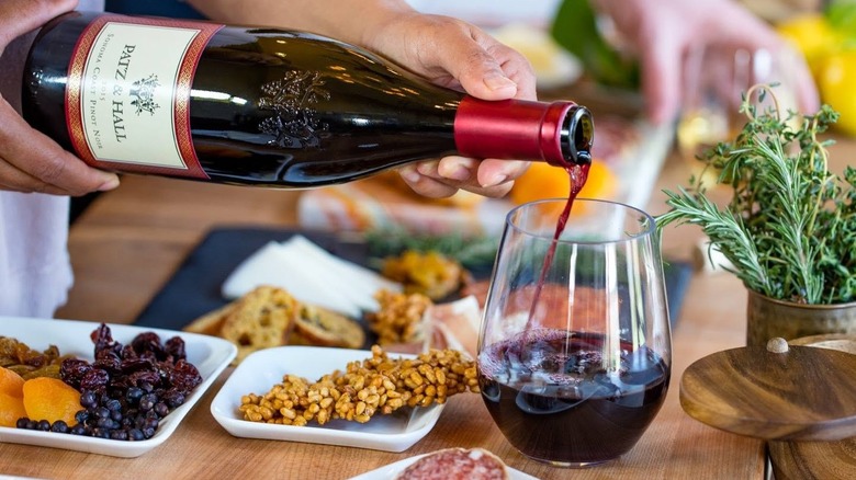 pouring bottle of red wine into glass with food