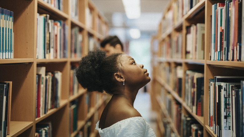 A woman in a library looking up at a bookshelf