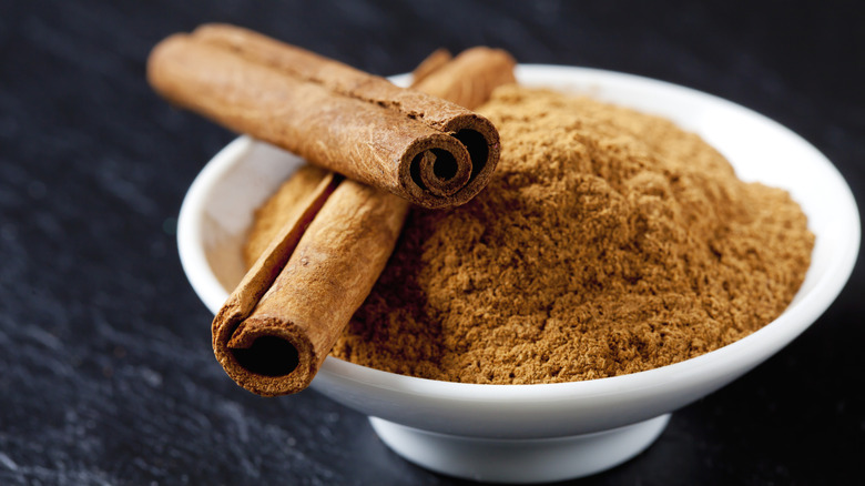 Bowl of ground cinnamon with two cinnamon sticks resting on top
