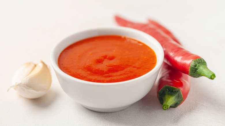 Hot sauce in bowl next to fresh red chili peppers and garlic clove