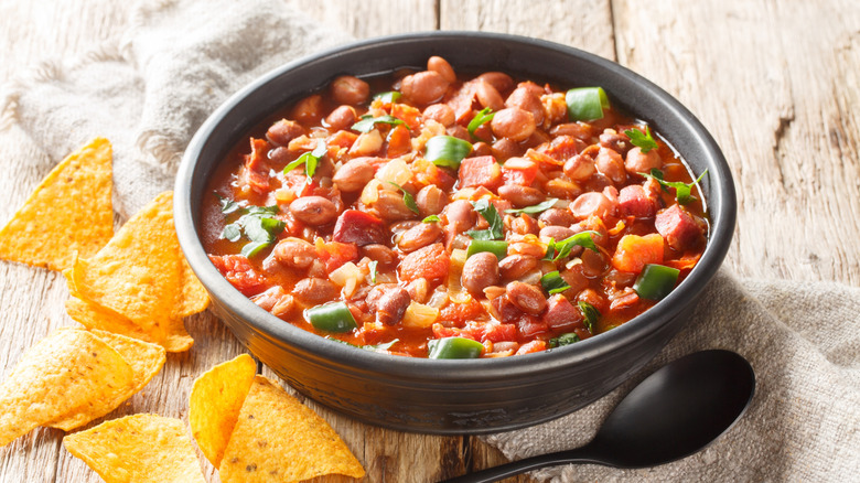 Pinto bean chili in black bowl next to tortilla chips