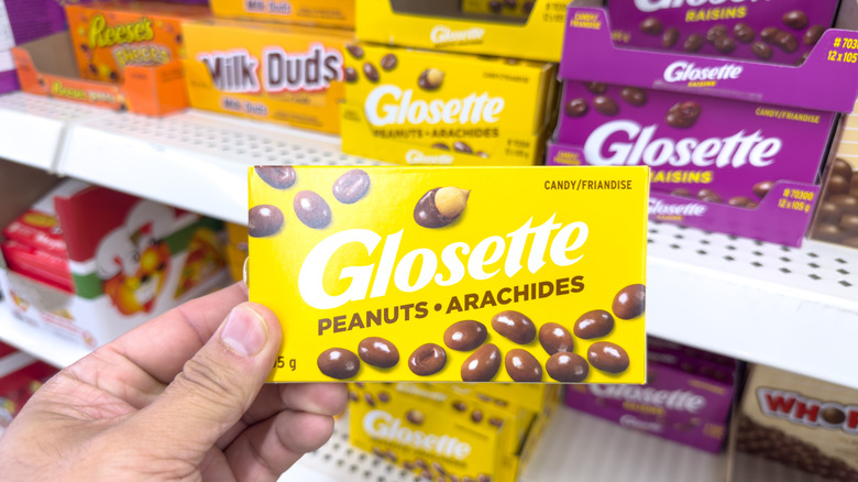 A view of a hand holding a package of Glosette chocolate covered peanuts, on display at a local grocery store.