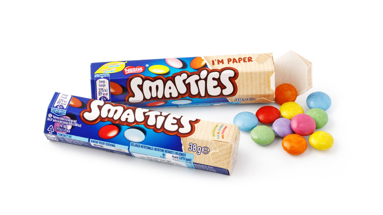 Smarties colorful chocolate candies spilling from a carton box on white background