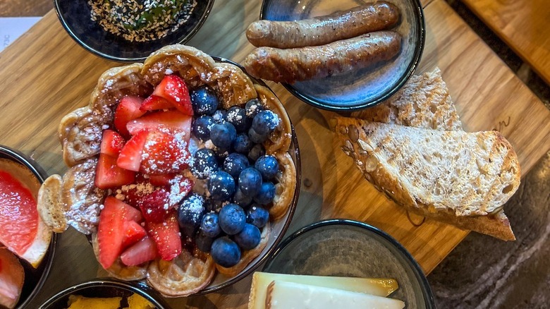 Danish waffles with strawberries and blueberries with brunch sides on wooden platter