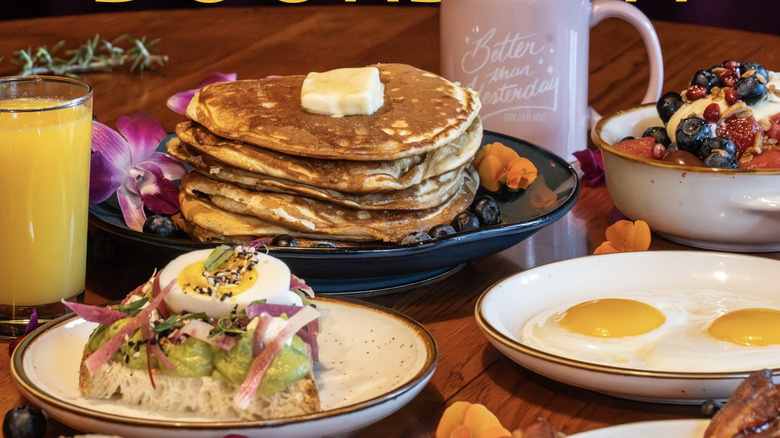 Brunch spread with pancakes, eggs, and avocado toast with drinks on a wooden table