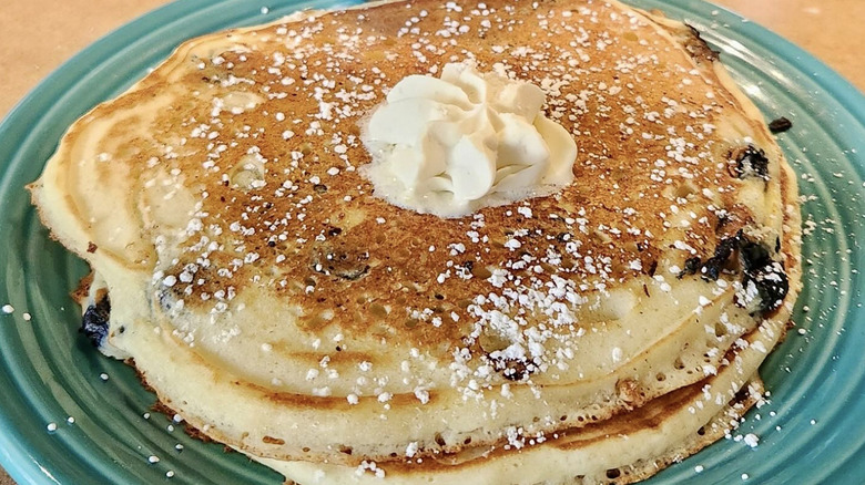 Stack of blueberry pancakes with whipped cream and powdered sugar on blue plate