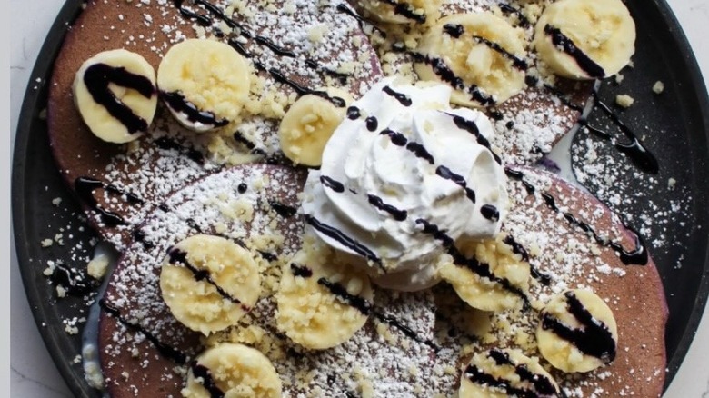 Ube and banana pancakes with whipped cream and powdered sugar for brunch