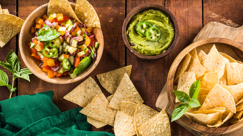 Top down view of bowls of salsa, guacamole, and tortilla chips on wooden table
