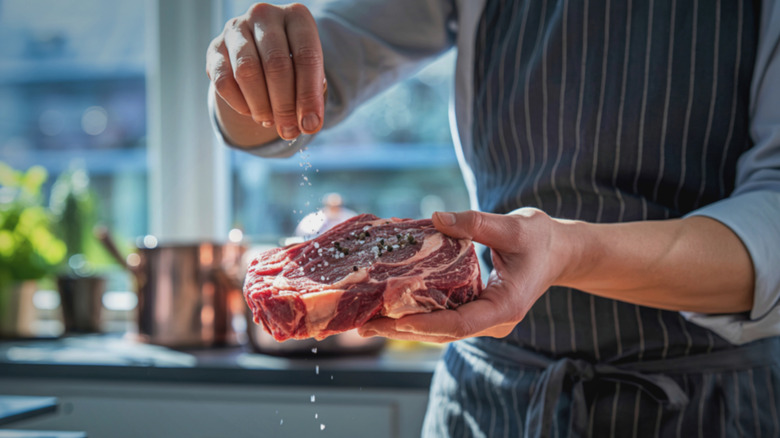 A person salting a raw cut of steak