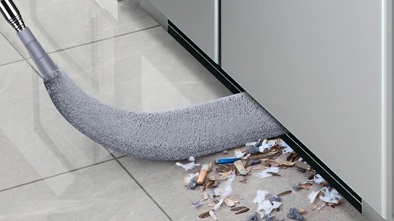 Gap cleaning tool reaching under cabinet to clean out trash