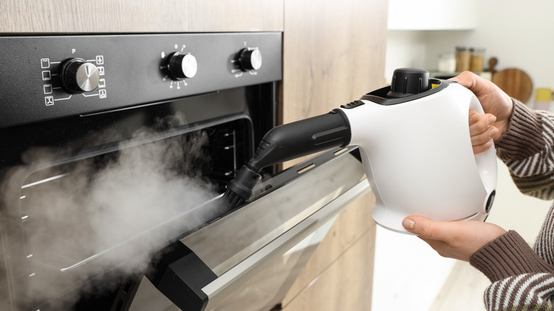 Hand holding a steam cleaner to steam clean the oven