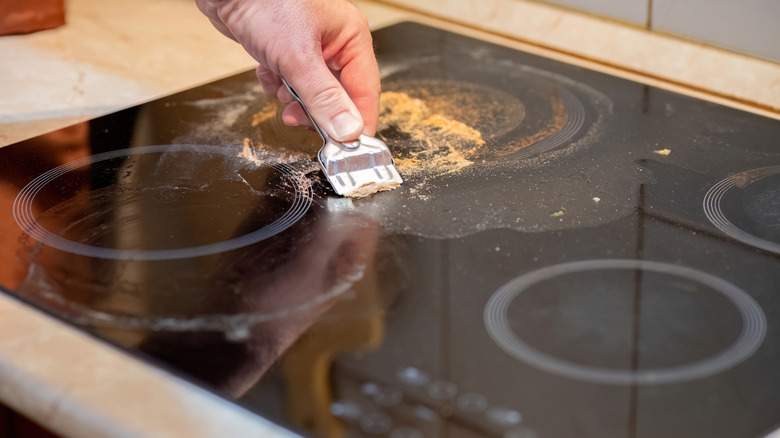 Hand using a scraper to clean a glass top range