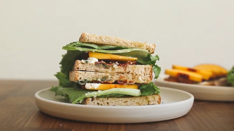 Bacon, lettuce, and peach sandwich stacked on white plate