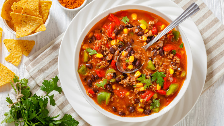 Bowl of ground beef taco soup with black beans and corn, next to fresh cilantro and bowl of tortilla chips