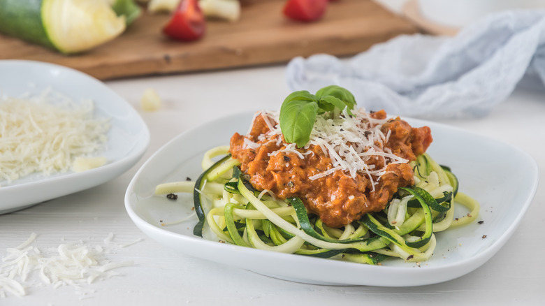 Plate of zucchini noodles topped with Bolognese sauce, shredded cheese, and sprig of basil