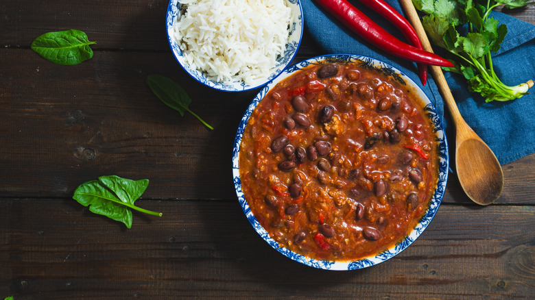 Bowl of chili and bowl of rice next to fresh red chili peppers and bunch of cilantro