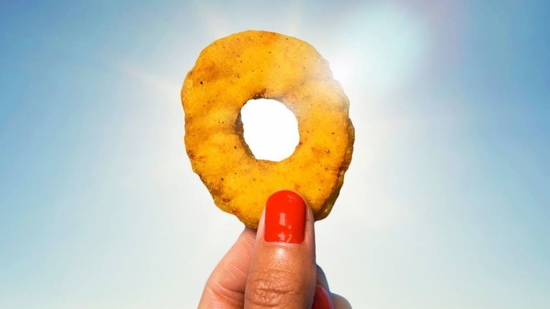 Fingers holding up a White Castle Chicken Ring against blue sky
