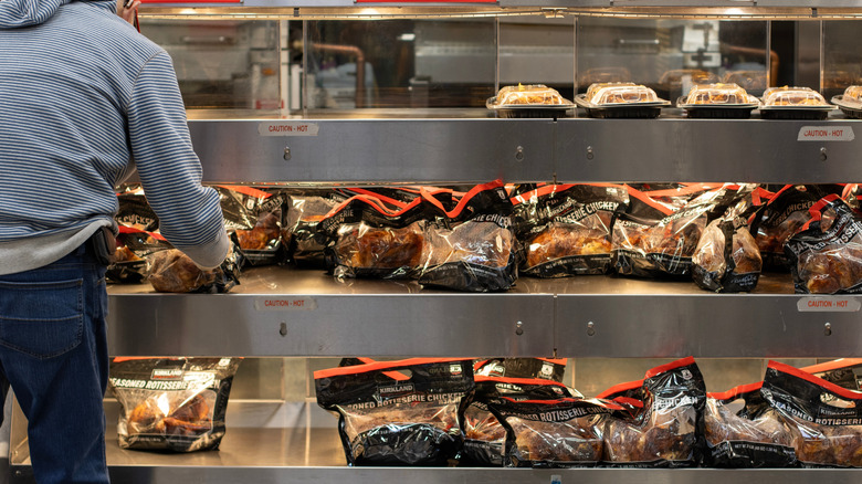 Man taking chicken from Costco's rotisserie chicken display
