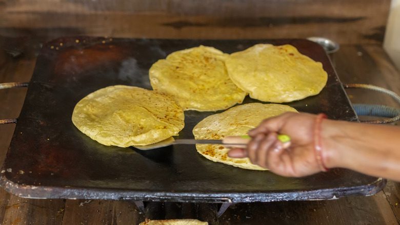 Hand flipping corn tortillas on large griddle