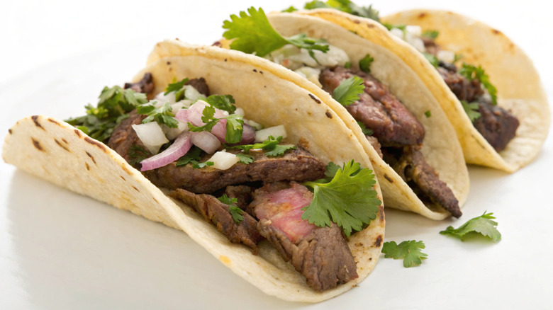 Overfilled carne asada tacos on white background