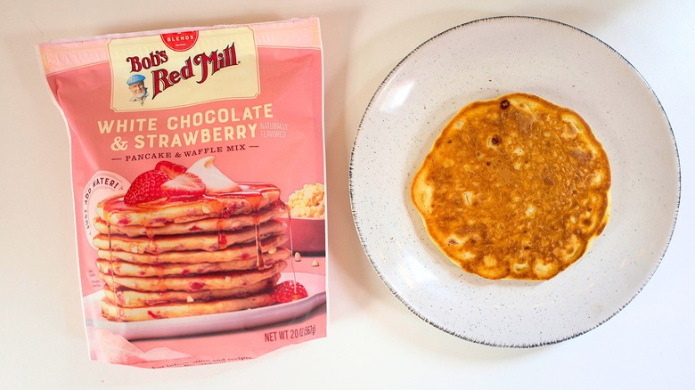 Overhead shot of bag of Bob's Red Mill White Chocolate Strawberry Pancake Mix next to pancake on white plate