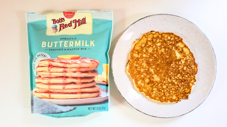 Overhead shot of bag of Bob's Red Mill Homestyle Buttermilk Pancake Mix next to pancake on white plate