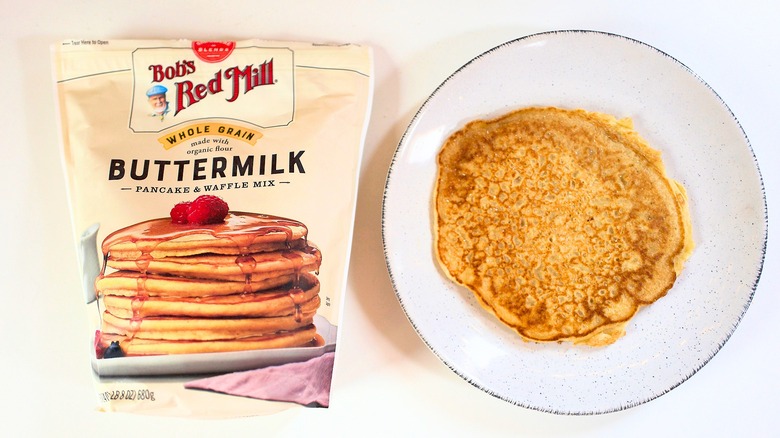Overhead shot of bag of Bob's Red Mill Whole Grain Buttermilk Pancake Mix next to pancake on white plate