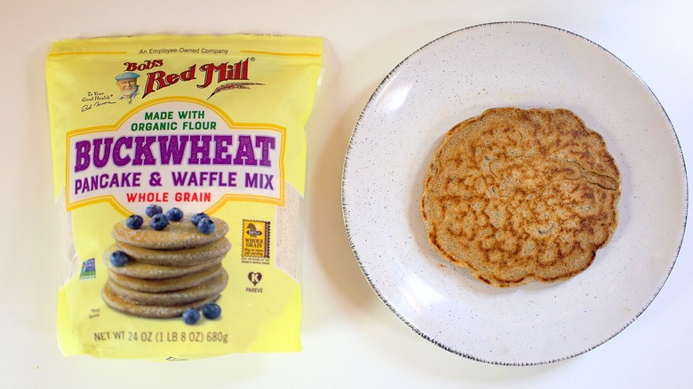 Overhead shot of bag of Bob's Red Mill Buckwheat Pancake Mix next to pancake on white plate