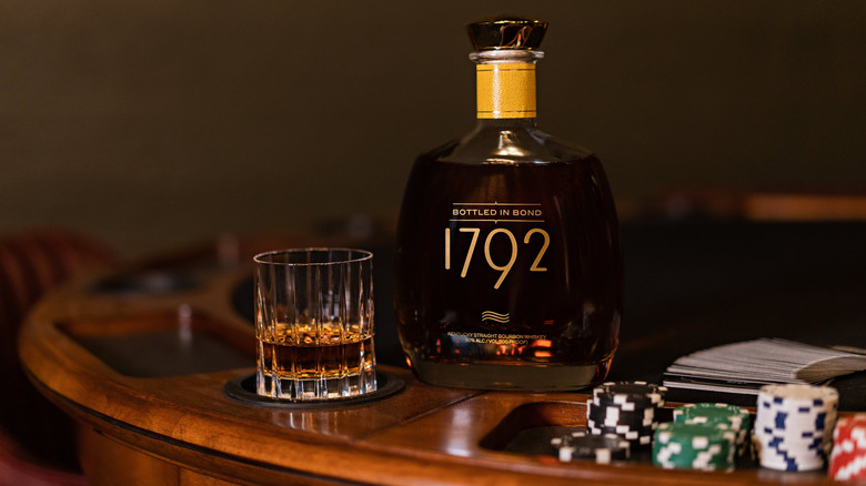 A 1792 Bottled-in-Bond bottle on a poker table beside poker chips and a filled glass