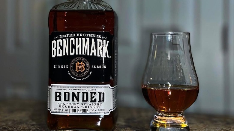 A close up of a Benchmark Bonded bottle beside a filled glass on a countertop