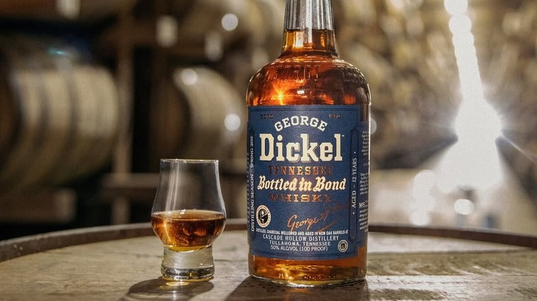 George Dickel Bottled-in-Bond posed on a whiskey barrel next to a filled glass