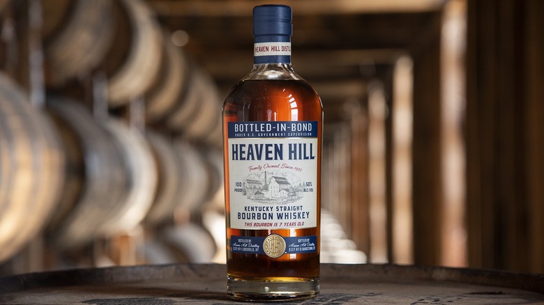 Heaven Hill Bottled-In-Bond bottle posed on top of a barrel with rows of barrels in the background