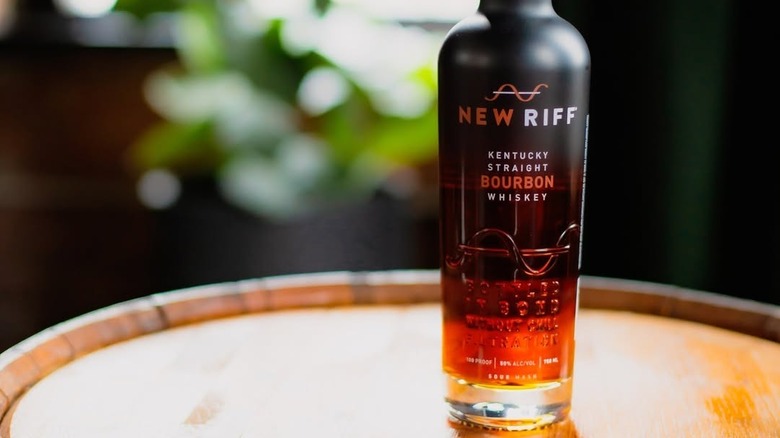 A close up of a New Riff Kentucky Straight Bourbon bottle on top of a barrel with a blurred background