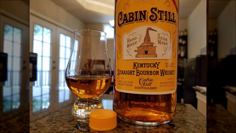 A close-up shot of a bottle of Cabin Still placed on a countertop next to a filled glass
