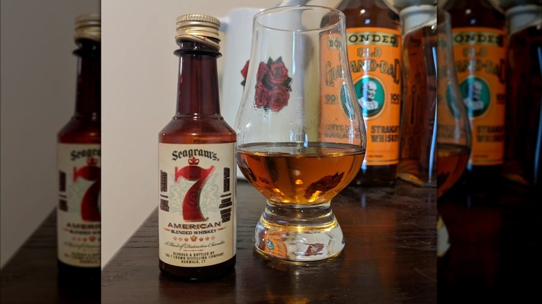 A small bottle of Seagram's 7 placed on a table next to a filled Glencairn glass