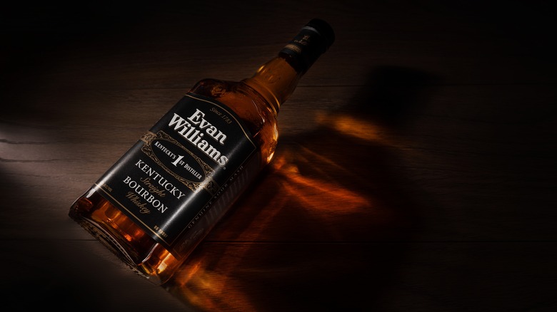 A bottle of Evan Williams laid on its side on a dark background with light shining through it