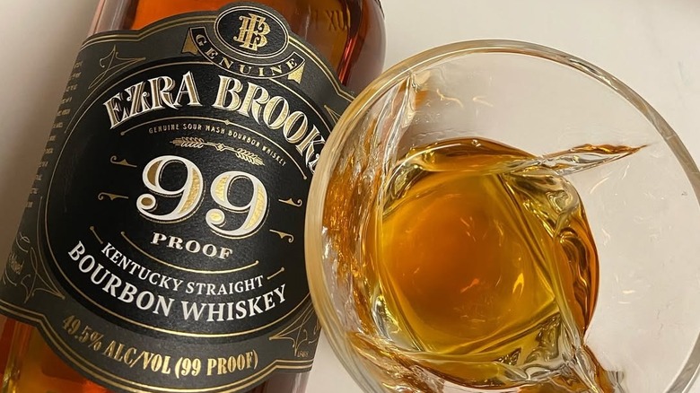 A close-up of a bottle of Ezra Brooks 99 Proof on its side alongside a filled whiskey glass