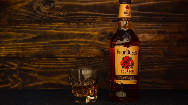 A bottle of Four Roses Yellow Label shown against a wooden background with a filled glass next to it