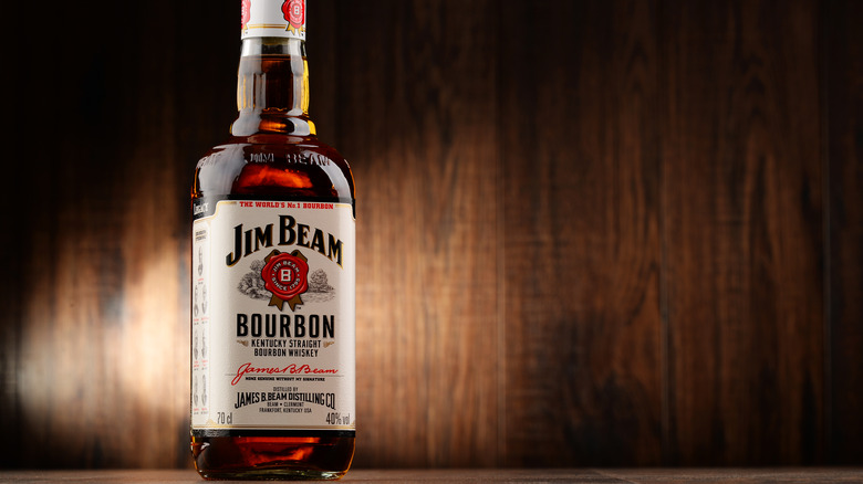 A bottle of Jim Beam stood up with a wooden background and a light shining though it