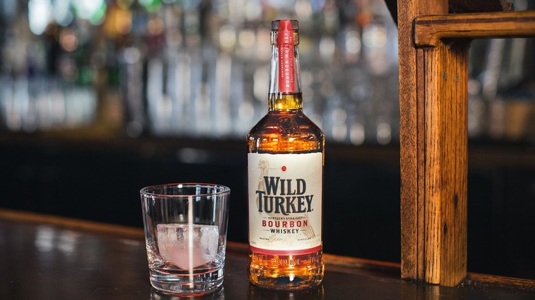 An unopened bottle of Wild Turkey shown on a bar with a glass and ice next to it