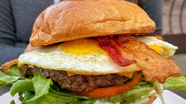 Bacon sticking out of burger with egg, lettuce, and tomato