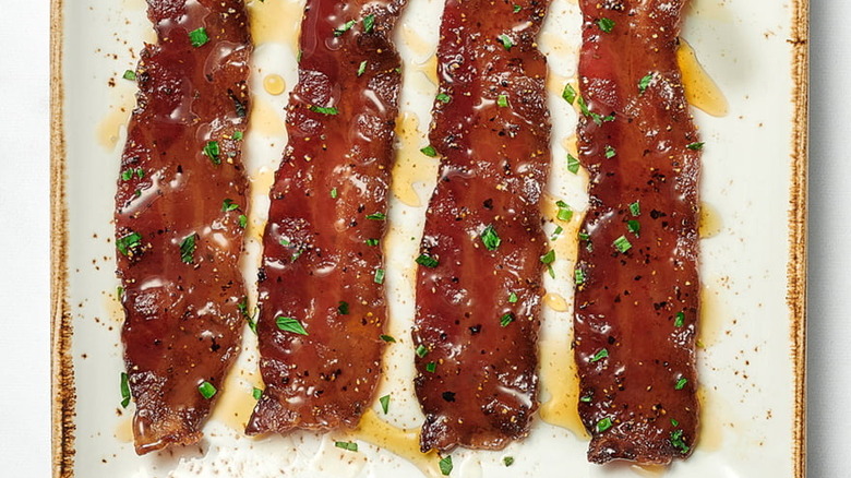 Four pieces of juicy cooked bacon with green herb garnish