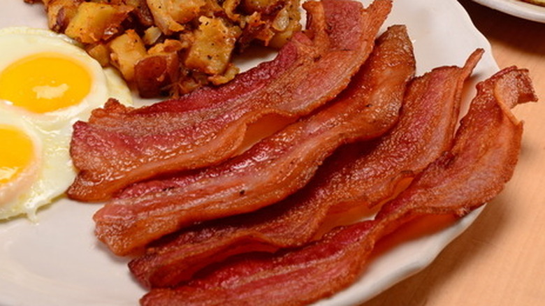 Four pieces of cooked bacon on plate with hashbrowns and eggs