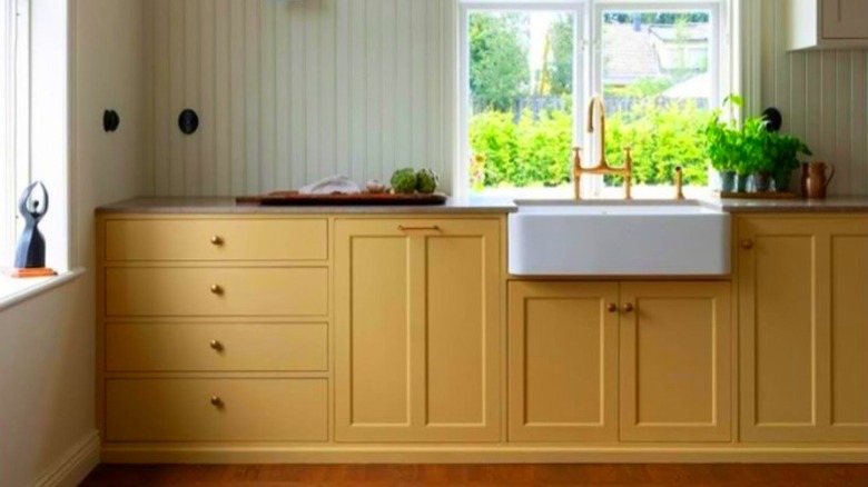 A kitchen with butter-yellow cabinets and white paneling