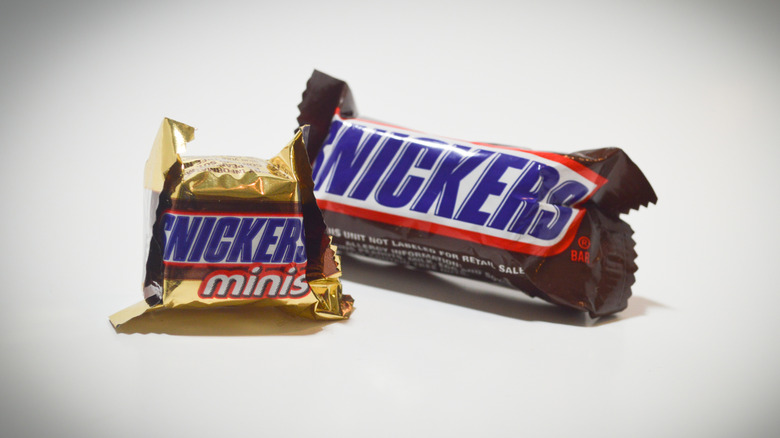 A mini Snickers candy bar in front of a bite size Snickers